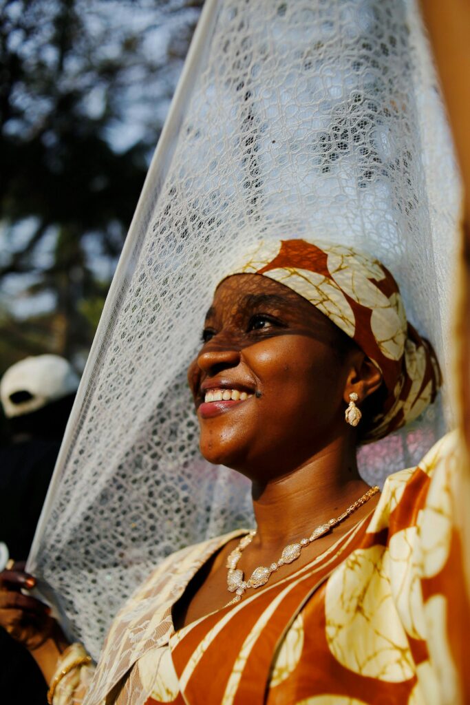 pexels-photo-30541280-30541280 A woman in traditional Nigerian attire smiles under the sun in an outdoor setting in Abuja, Nigeria.